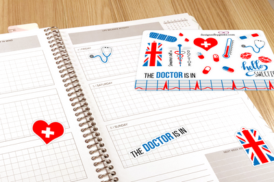 An open planner sits on a wood surface. On top of the planner is a sticker sheet with medical/Doctor Who themed stickers in red, blue, white, and grey. Some stickers have been added the planner: heart, stethoscope, Union Jack phone box, "The Doctor is In"