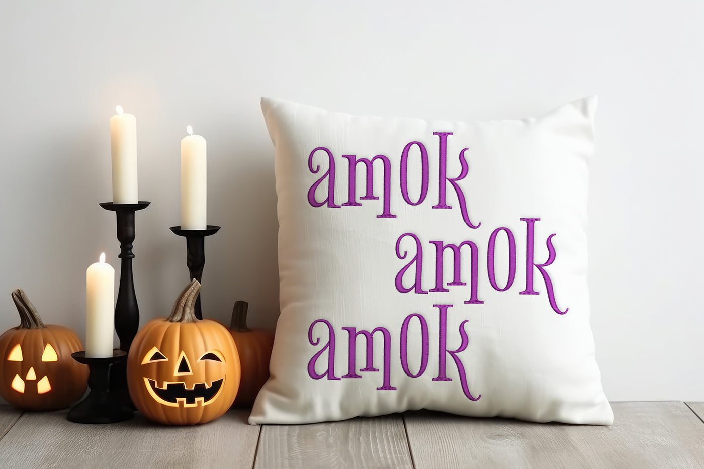 Decorative pillow with 'amok' text, pumpkins, and candles on a wooden floor.