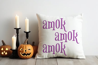 Decorative pillow with 'amok' text, pumpkins, and candles on a wooden floor.