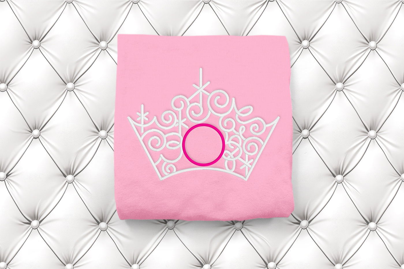 Pink fabric with a white crown design and pink circular monogram frame on a textured white background
