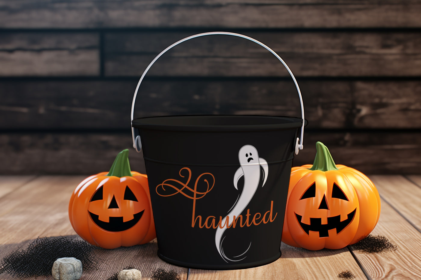 Black Halloween bucket with ghost design and 'haunted' text, surrounded by carved pumpkins on a wooden surface.