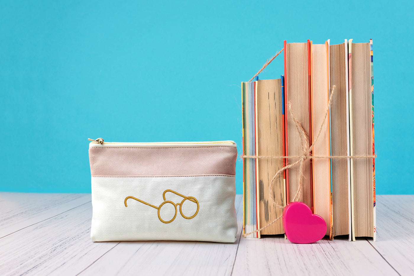 Small pouch with angled glasses embroidery design next to books on a wooden surface with a blue background
