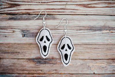 Pair of ghost face earrings on a wooden surface