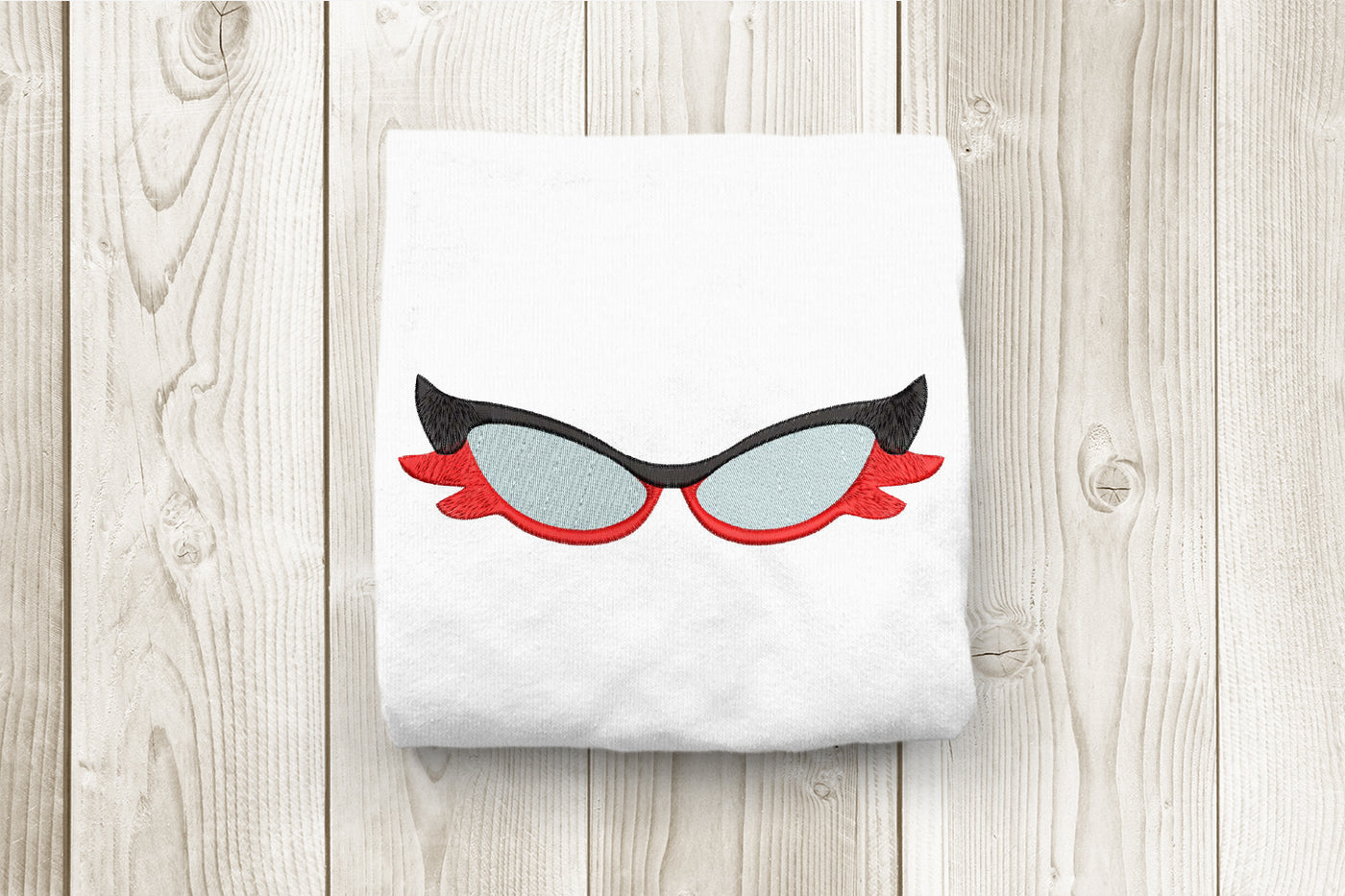 White towel with cat-eye sunglasses embroidery design on a wooden surface