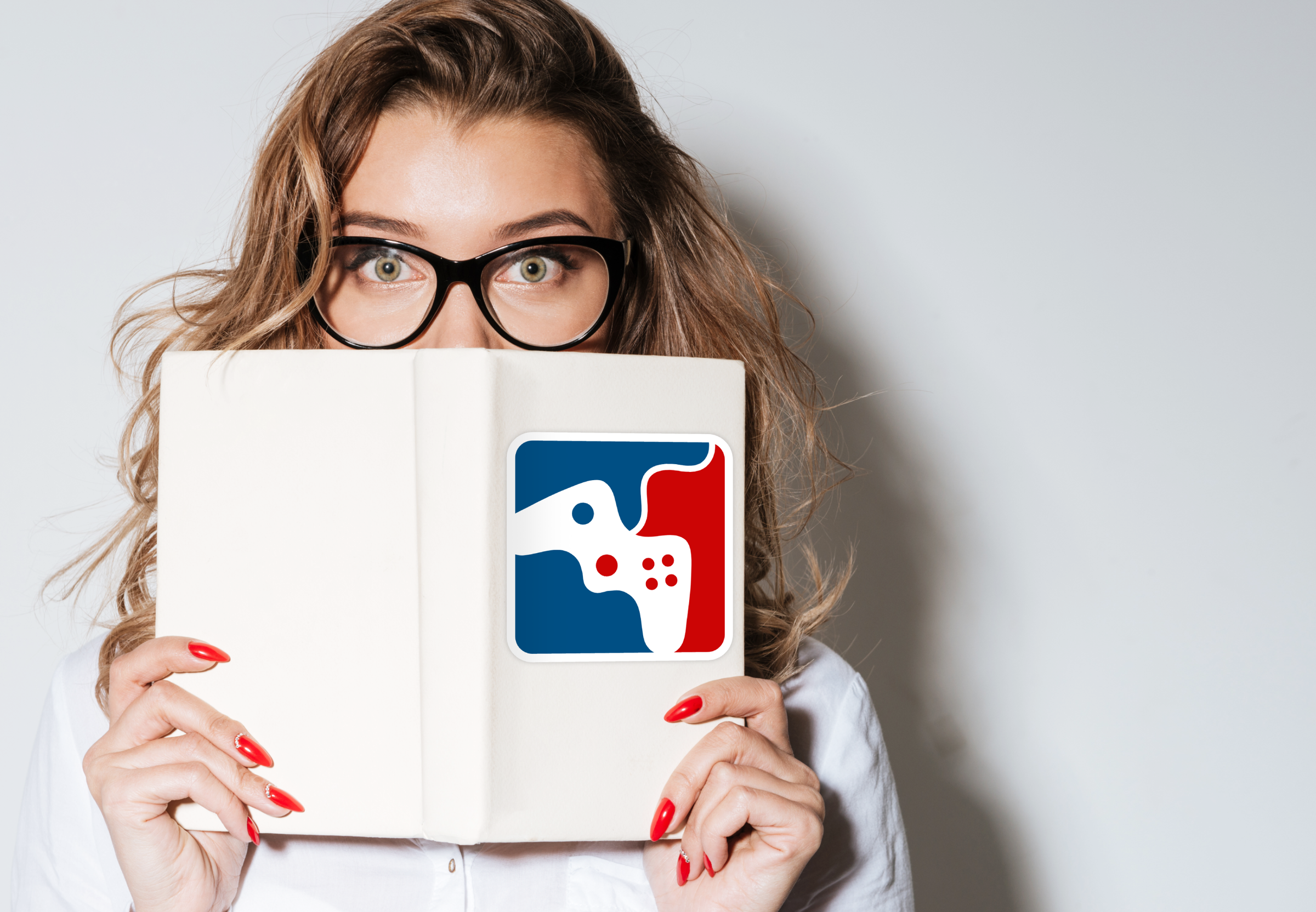 A white women with glasses is holding an open offwhite journal in front of her face. The journal has a square design in red, blue, and white that parodies a sports logo but with a video game controller. She stands in front of a white wall.