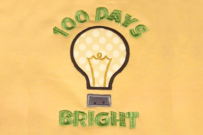 Applique light bulb on pale yellow fabric with embroidered words in green saying "100 days bright"