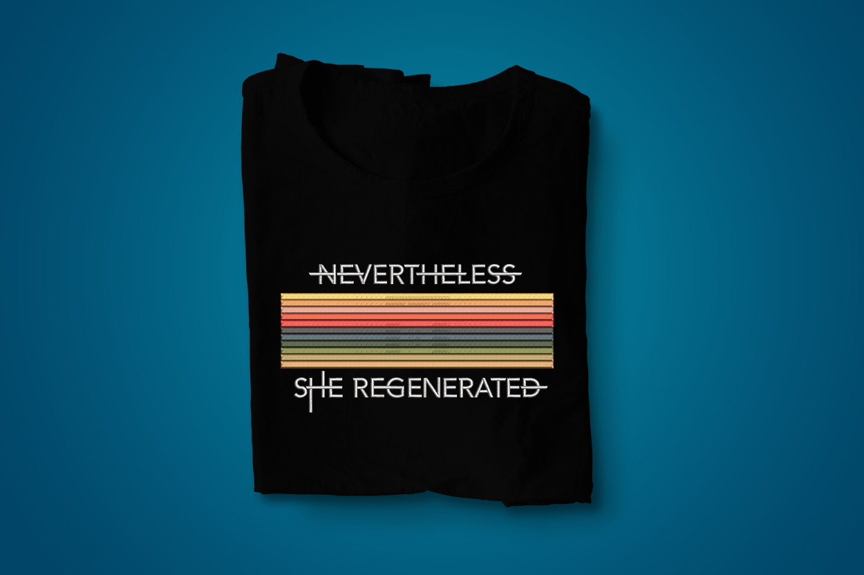 A folded black tee with horizontal multi-color satin stitch stripes. Above and below the stripes are the words "Nevertheless she regenerated."