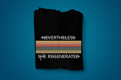 A folded black tee with horizontal multi-color embroidered stripes. Above and below the stripes are the words "Nevertheless she regenerated."