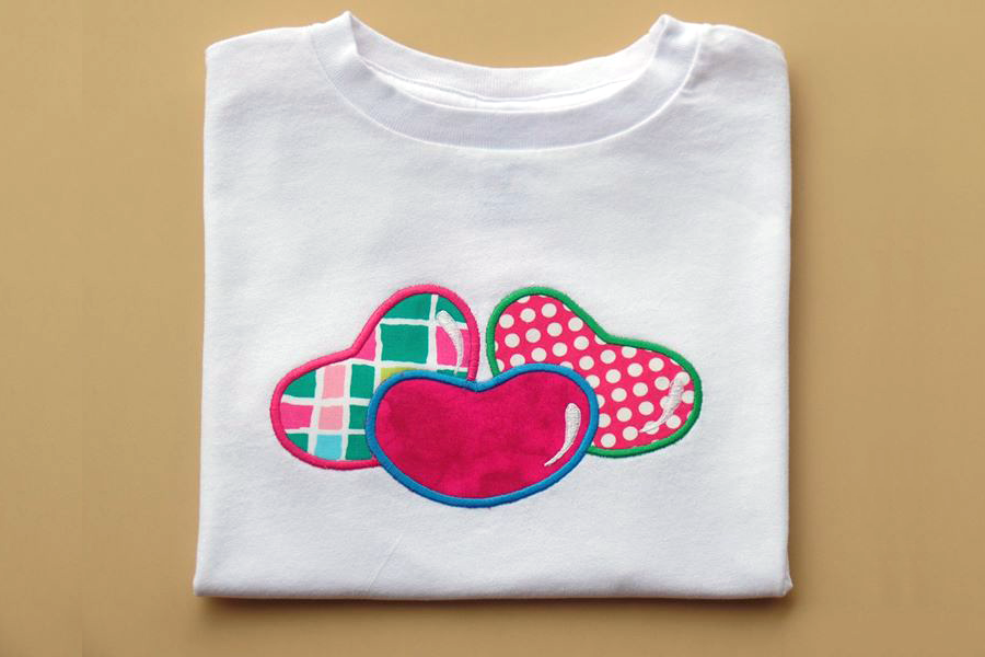 3 applique jelly beans in brightly colored patterned fabric on a white folded tee.