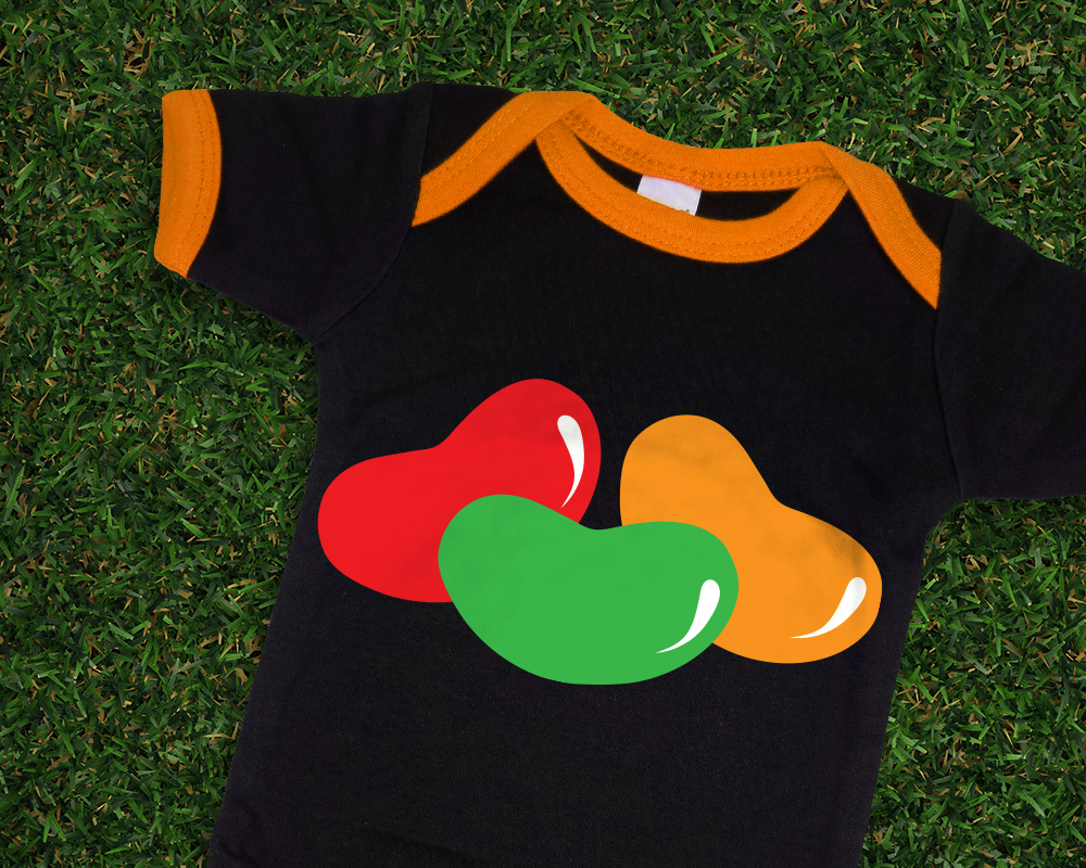 A black and orange ringer tee style baby onesie sits on some grass. It has 3 large jelly beans in red, green, and orange.
