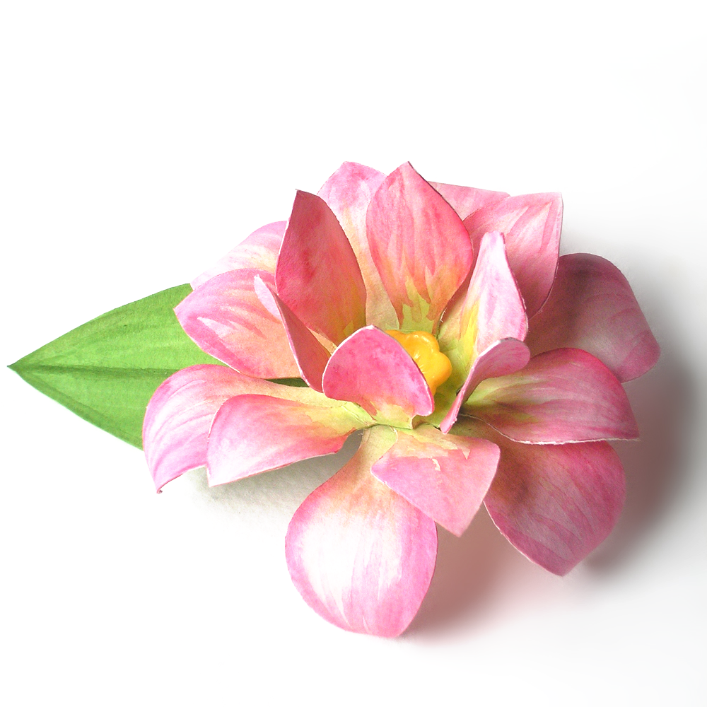 A lotus flower sculpted out of paper and painted with pink watercolor paint with a yellow button for the center. The flower also has a green sculpted paper leaf and sits on a white background.