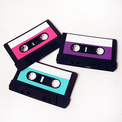 Three 3-dimensional paper cassette tapes with labels in pink, turquoise, and purple lay on a white background.