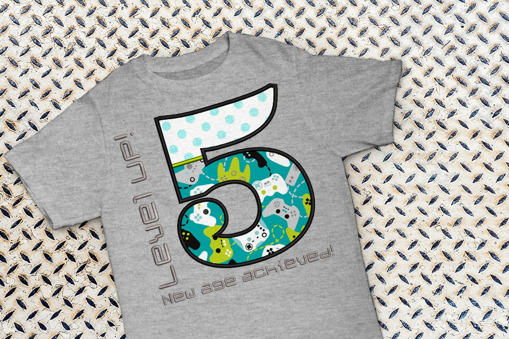 Shirt with large applique 5. Around the number is embroidered "Level UP! New age achieved!"