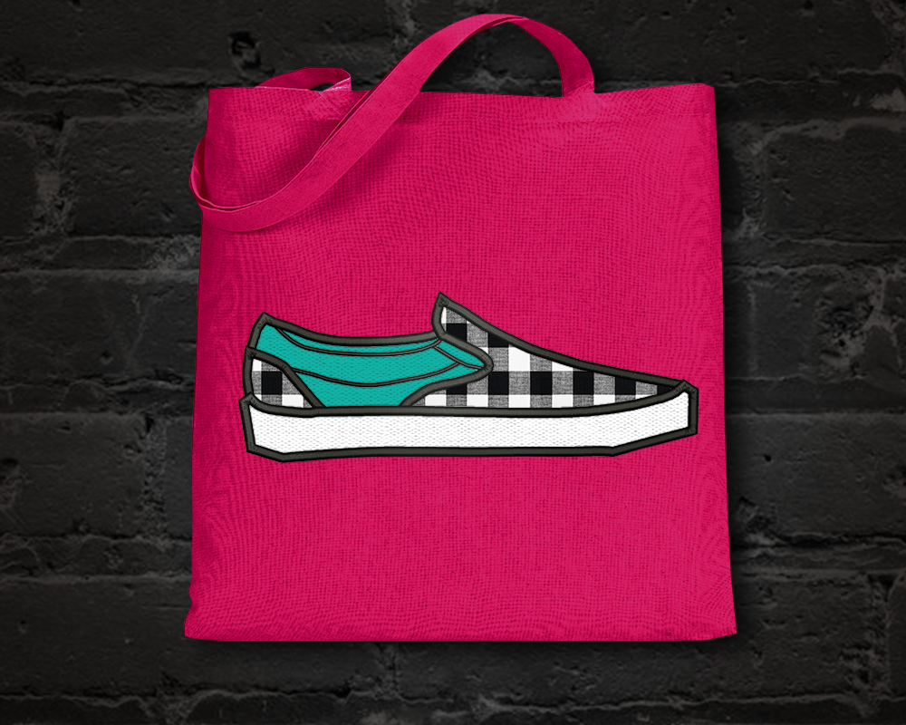 A hot pink tote bag on a black brick background. The tote has an applique design of a Vans style skater shoe done in turquoise and black gingham fabric.