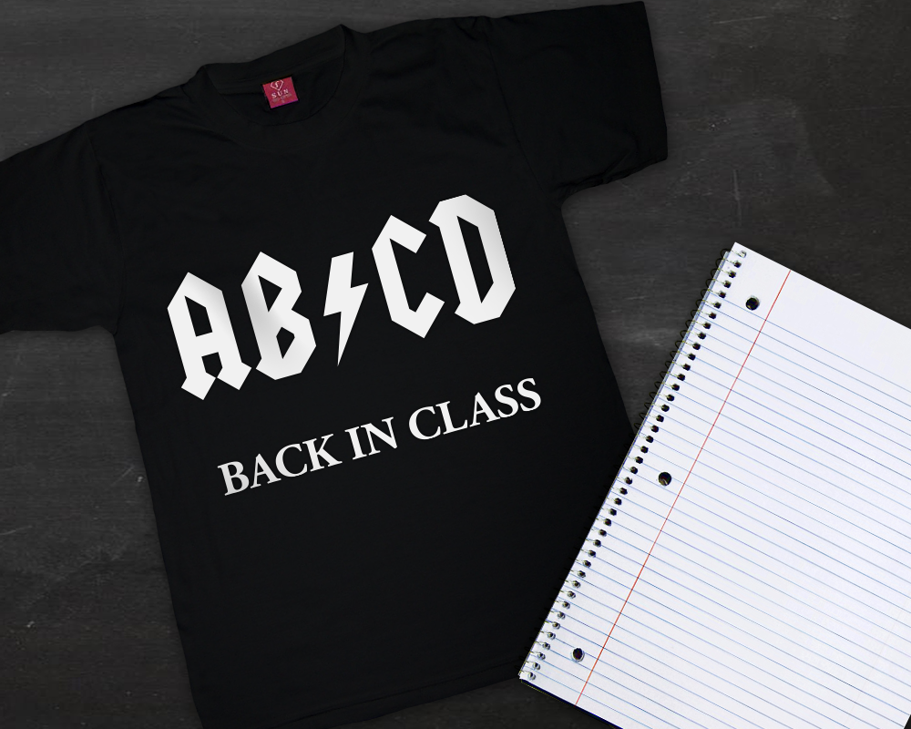 A black child's shirt and a spiral notebook sit on a chalkboard backdrop. The shirt says "AB/CD Back in Class" in white. The slash is a lightning bolt, a parody of the AC/DC logo.