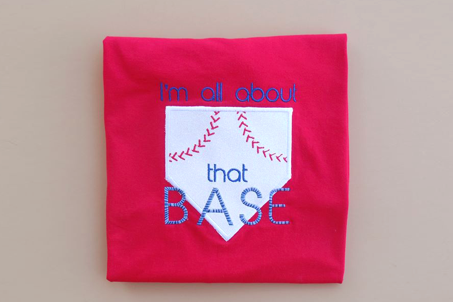 Applique of a home plate with red baseball style stitching and the embroidered words "I'm all about that base."
