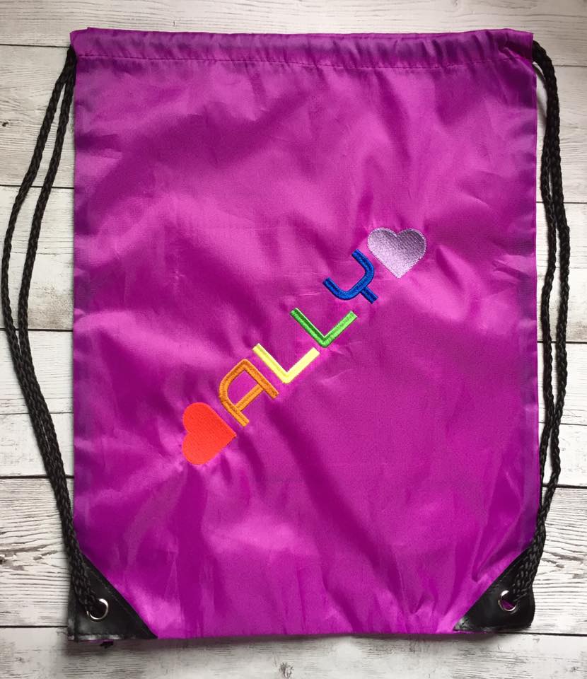 Drawstring bag with the word "Ally" and a heart at each side embroidered in rainbow colors.