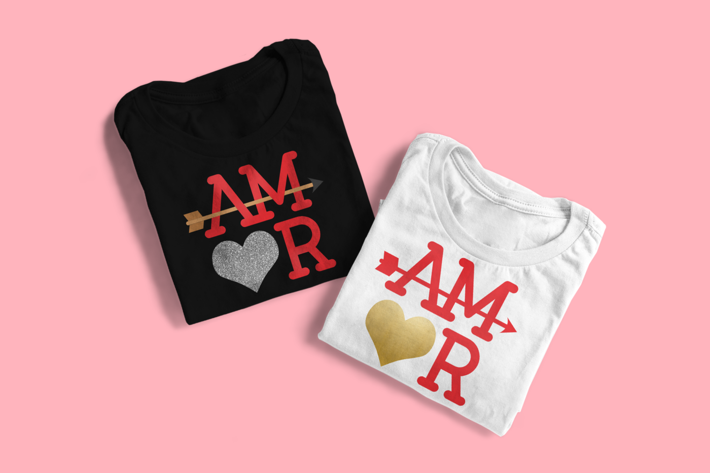 A black and white folded tee sit on a pink background. Each has the word "AMOR" set on a square, with a heart for the O and an arrow running through the A and M.