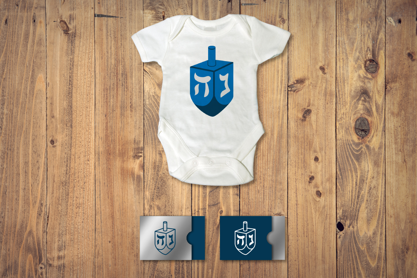 A baby onesie with two gift card holders below. Each has a dreidel design.