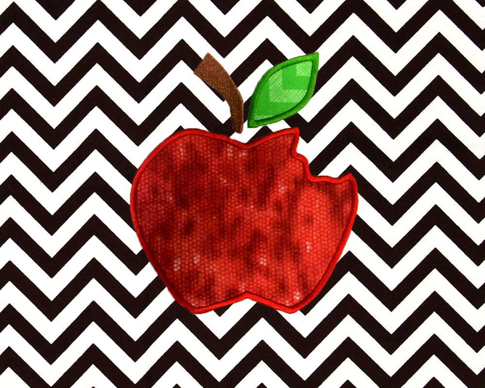 A piece of black and white chevron fabric has an applique apple with a bite out of it embroidered onto it.
