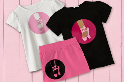 Two kid's shirts and a skirt are on a pink painted wood backdrop. Each shirt has an image of a pair of feet wearing pointe ballet slippers set inside of a circle.