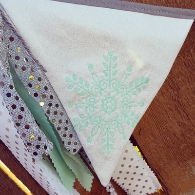 An intricate aqua snowflake embroidery on white triangle bunting flag.