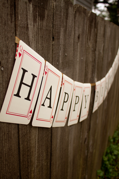 Playing card banner with Queen of Hearts card that says "Happy Birthday" hanging from a fence.
