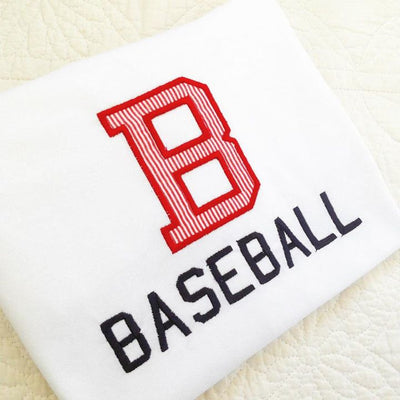 A white folded shirt sits on a white background. Embroidered onto the shirt is the word "Baseball" and a large applique B above in red and white striped fabric.