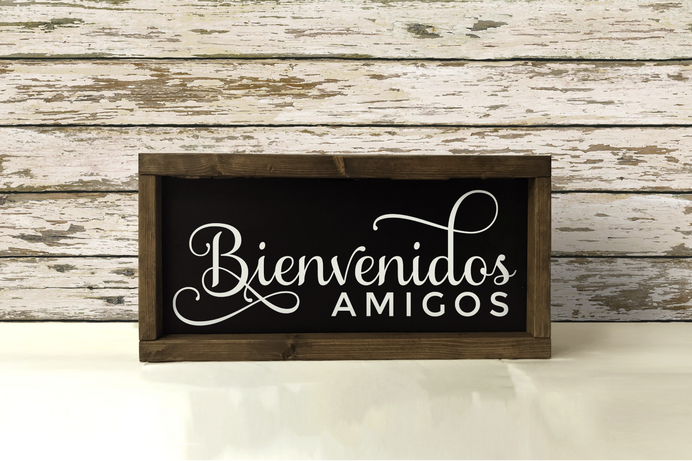 A wood framed sign that is black with white letters. The sign says "Bienvenidos amigos."