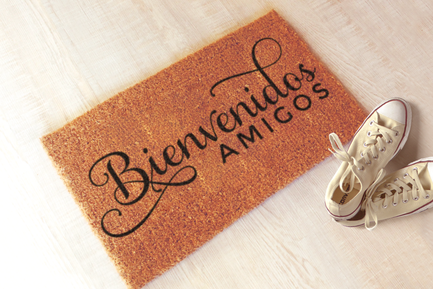 A doormat with a pair of ivory converse laying nearby. The doormat says "Bienvenidos amigos."