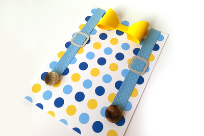 A card with a blue and yellow polkadot print with blue paper suspenders with real buttons at the end and a 3D yellow paper bow tie.