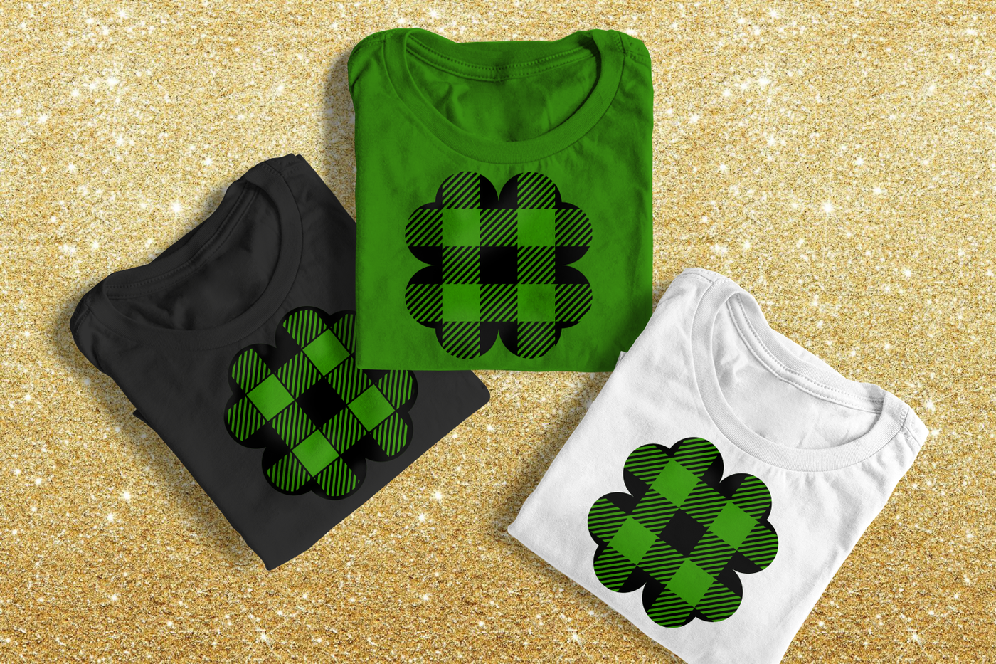 Three folded shirts on a glitter gold background. Each has a 4 leaf clover on it with a buffalo plaid pattern.