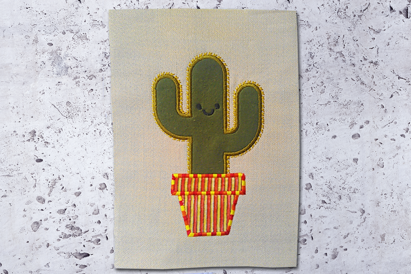 A green cactus in a pot is embroidered onto a piece of natural canvas fabric. The applique fabric for the pot is striped. Around the applique of the cactus are embroidered spines.