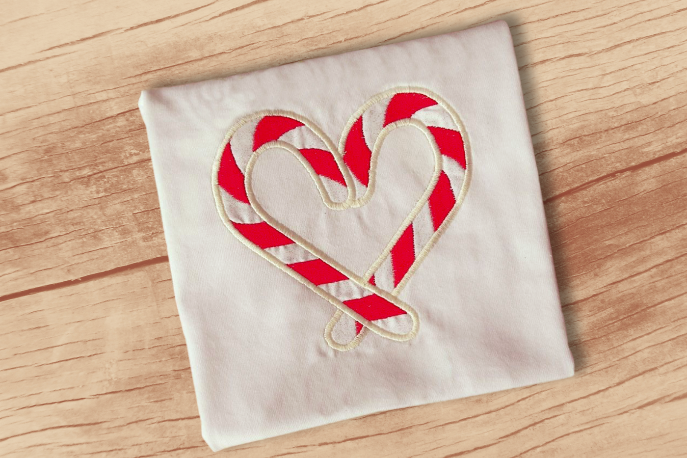 A white square of fabric has a heart applique design. The heart is formed by two red and white striped candy canes.