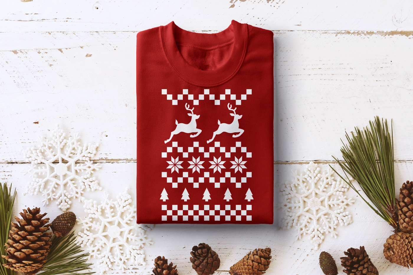 A folded red sweatshirt. On the shirt, done in the style of a Christmas sweater, are a checkerboard pattern, jumping reindeer, trees, and 8-pointed stars shapes.