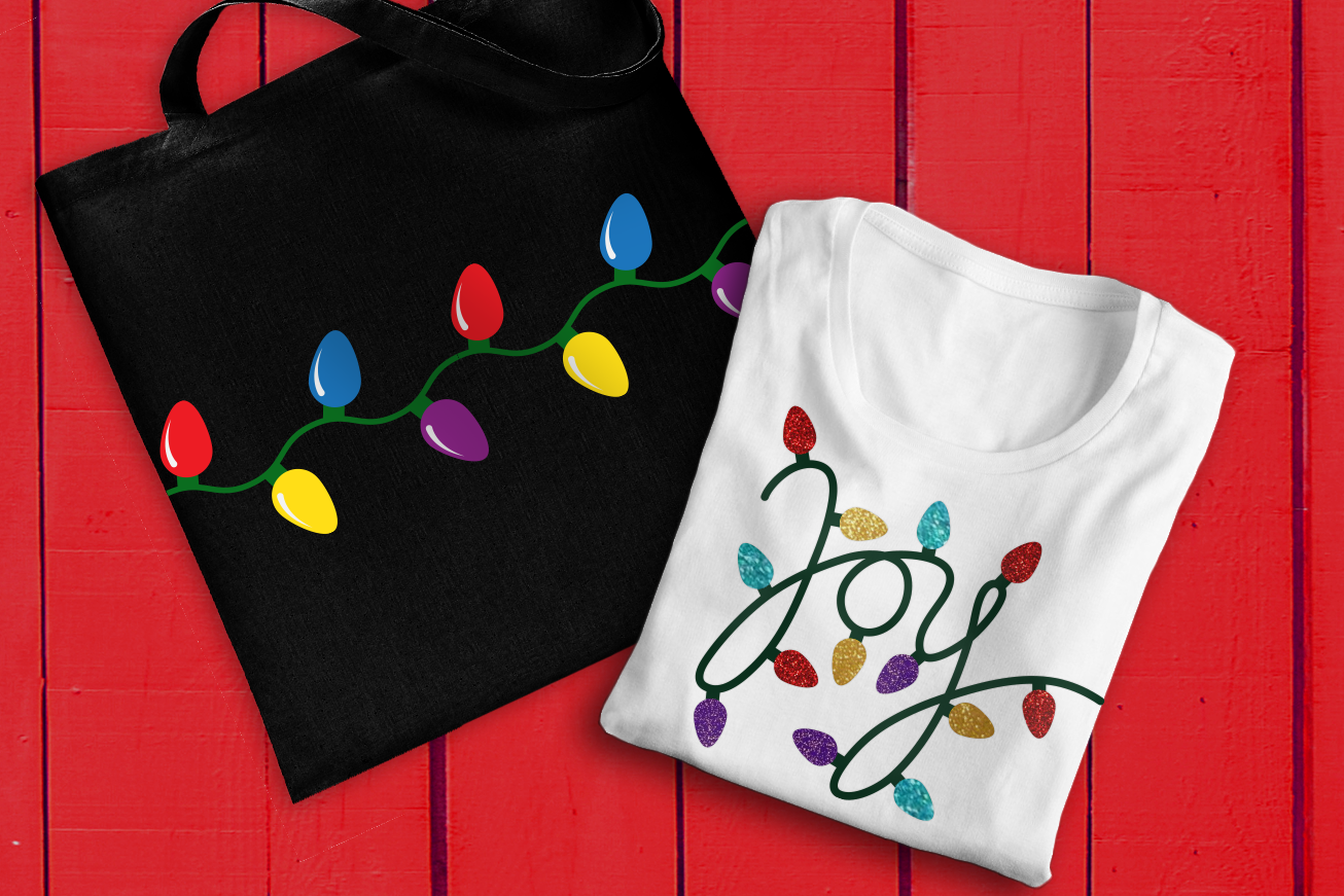 Tote bag with a string of Christmas lights design, and a folded tee with the word "Joy" spelled out of Christmas lights.