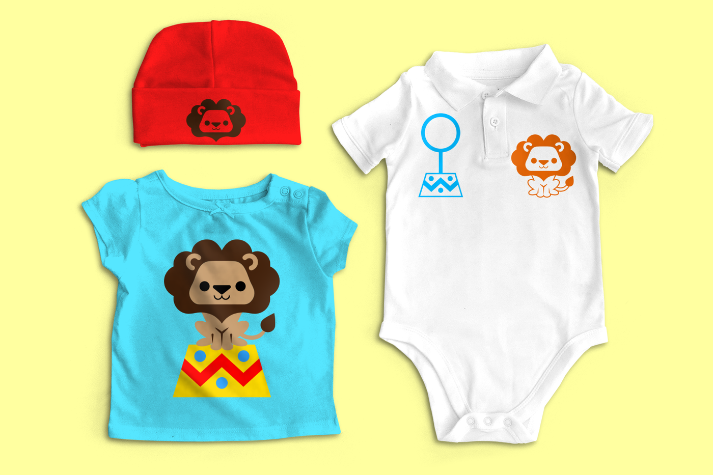 A set of baby clothes on a yellow background. A blue baby tee has a cute circus lion on a stand. A red baby cap has a lion's face. A white polo onesie has a lion on one side and a hoop on a stand on the other.