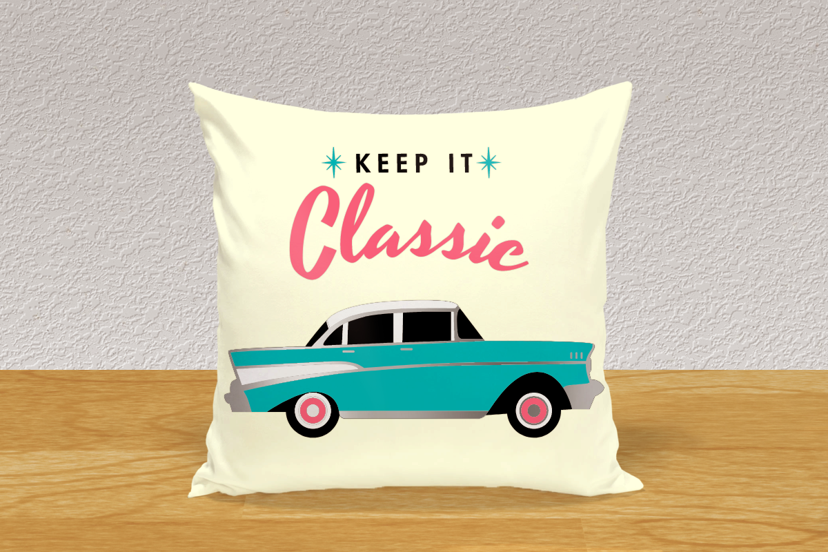 Cream throw pillow on wood floor against light grey wall. Has a classic 1950s car in turquoise with the words "keep it classic" above in 50s style lettering.