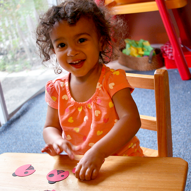 Black toddler plays with paper ladybugs on a table. Each ladybug has a number on its back and a different number of spots.