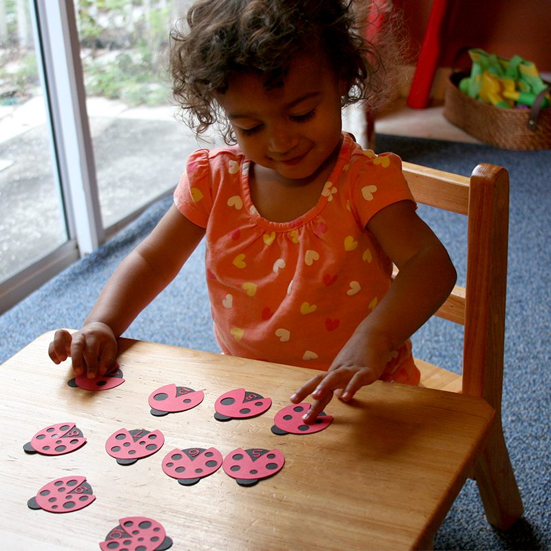 Black toddler plays with paper ladybugs on a table. Each ladybug has a number on its back and a different number of spots.