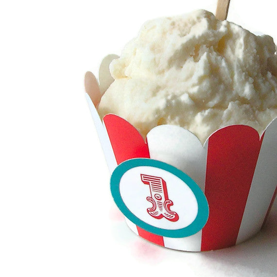 A vanilla frosted cupcake with a red and white striped scallop wrapper. A circle pops out from the cupcake that has a turquoise outline and red number 1 in the middle in circus style lettering.