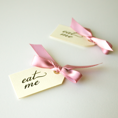 Two ivory tags with pink bows that each say "eat me."