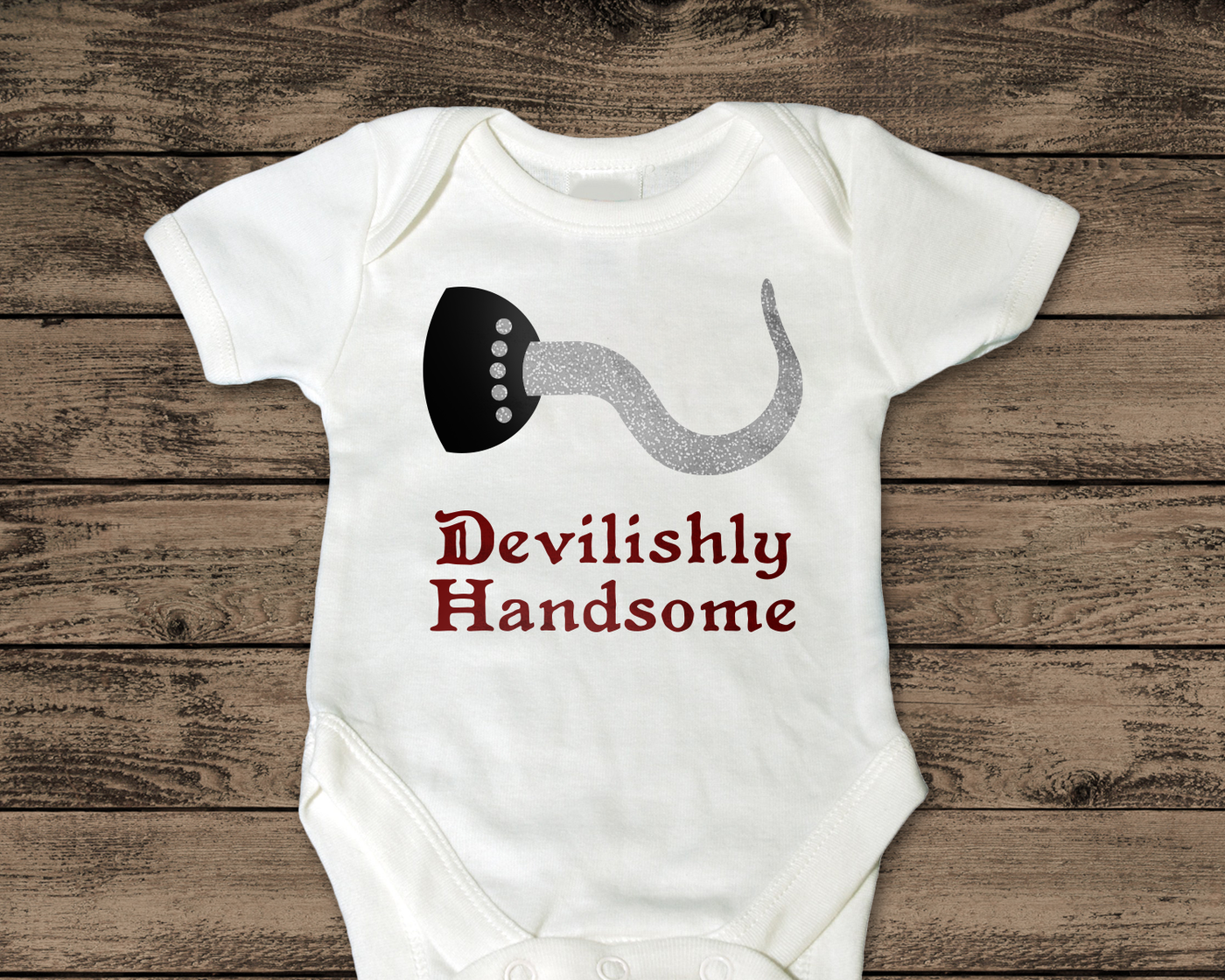 A white baby onesie with the words "Devilishly Handsome" with a pirate hook above.