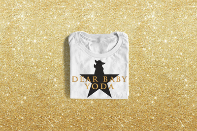 A shirt embroidered with a star. The top of the star is replaced by an alien baby. In front are embroidered the words "Dear Baby Yoda."