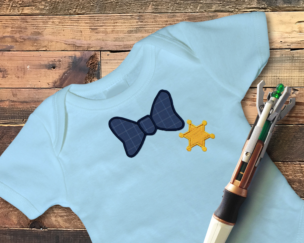 A blue baby onesie with an applique bow tie and sheriff badge. The 11th Doctor's sonic lays on top.