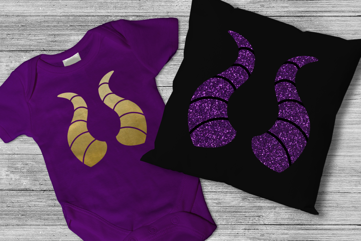 A purple baby onesie and black throw pillow, each with a dragon horn design.