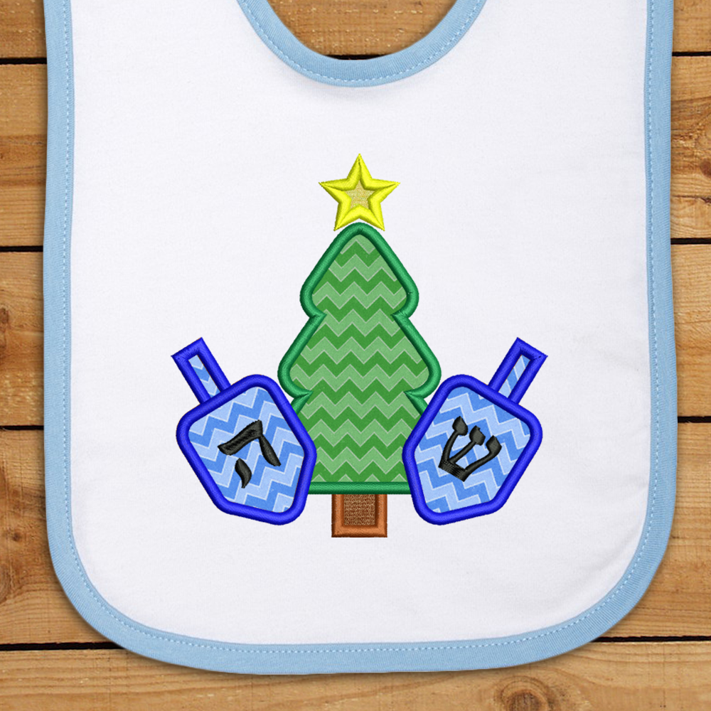 A bib decorated with the applique design of a Christmas tree with a dreidel on each side.