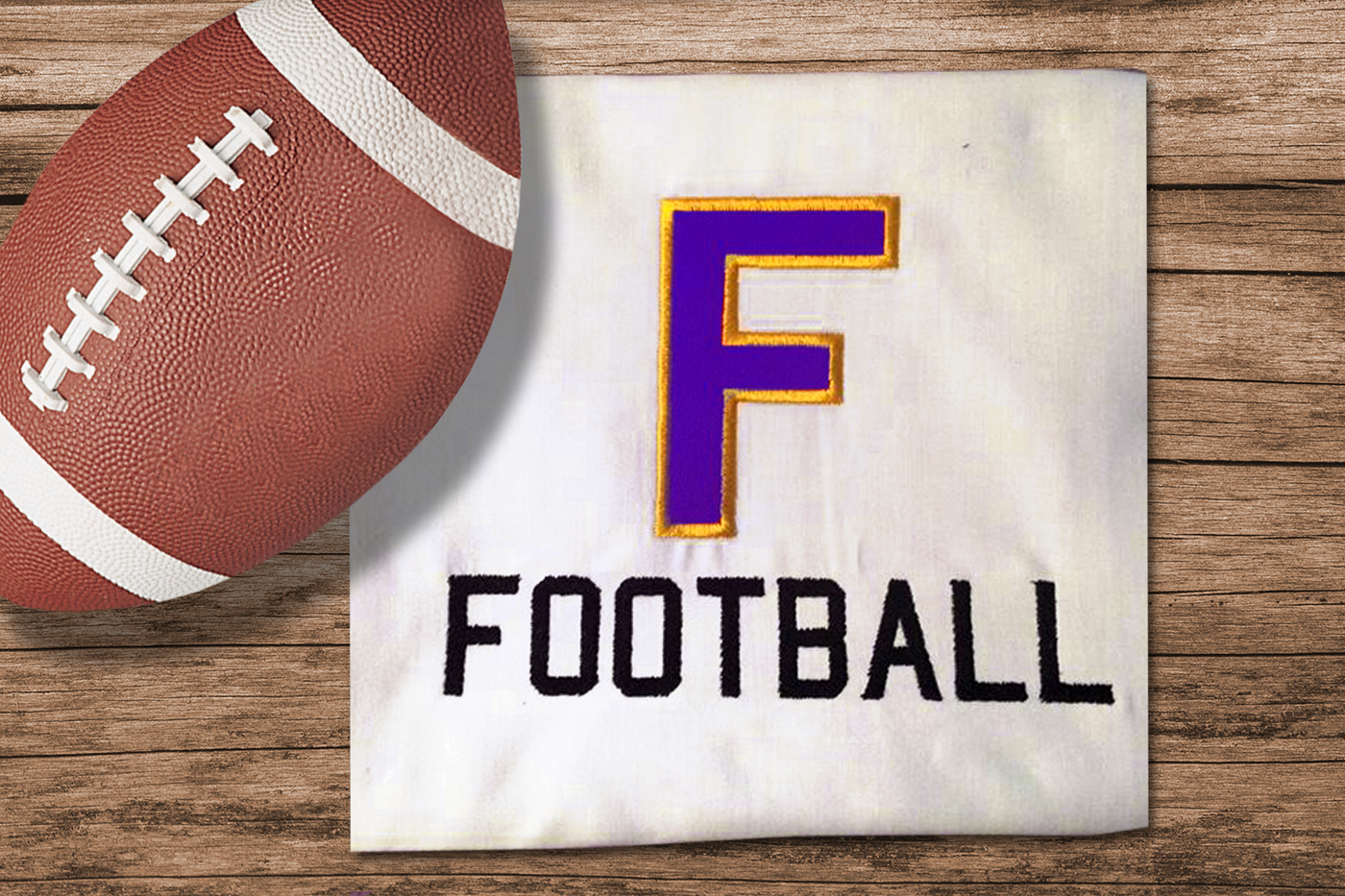 A folded white tee with a football laying on top. Embroidered onto the shirt is the word "FOOTBALL" with a large applique letter F above.
