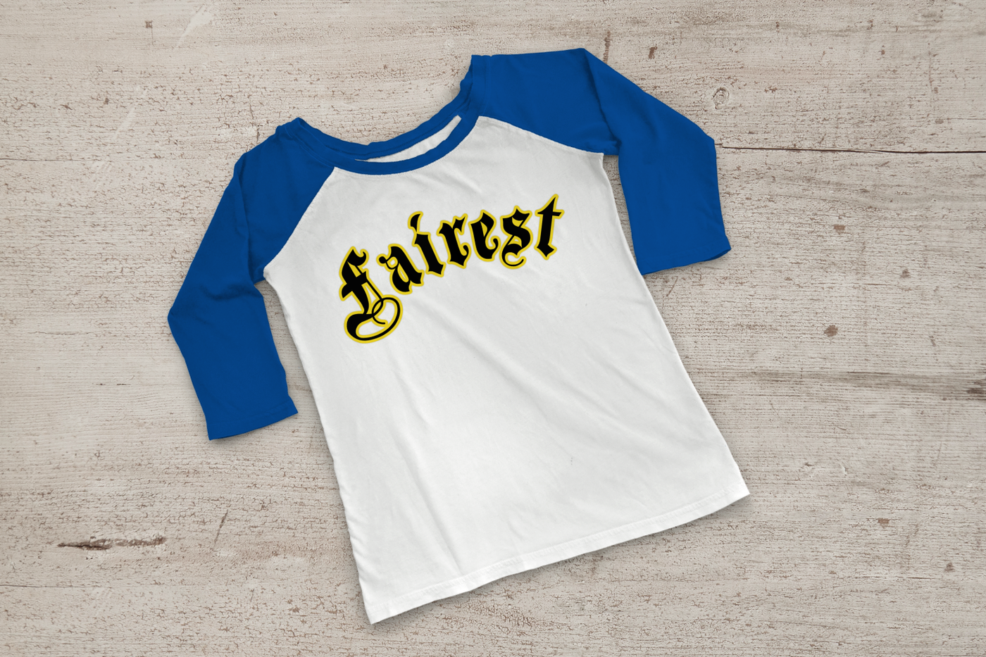 Blue and white raglan tee with the word "fairest" in a fairy tale blackletter font with a yellow offset outline.