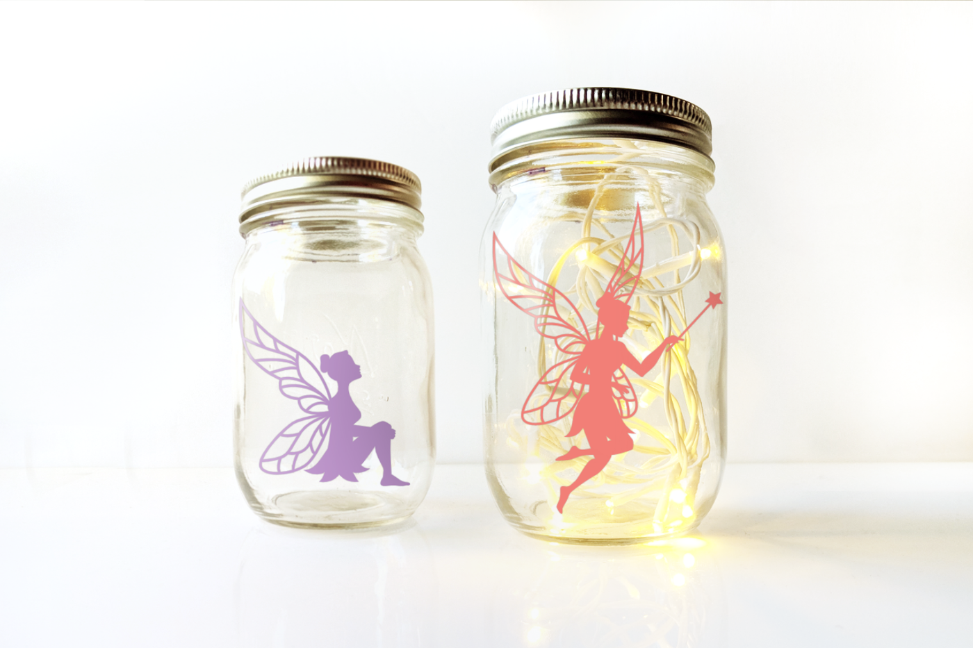 Two canning jars, each with a different fairy silhouette. One jar has fairy lights inside.
